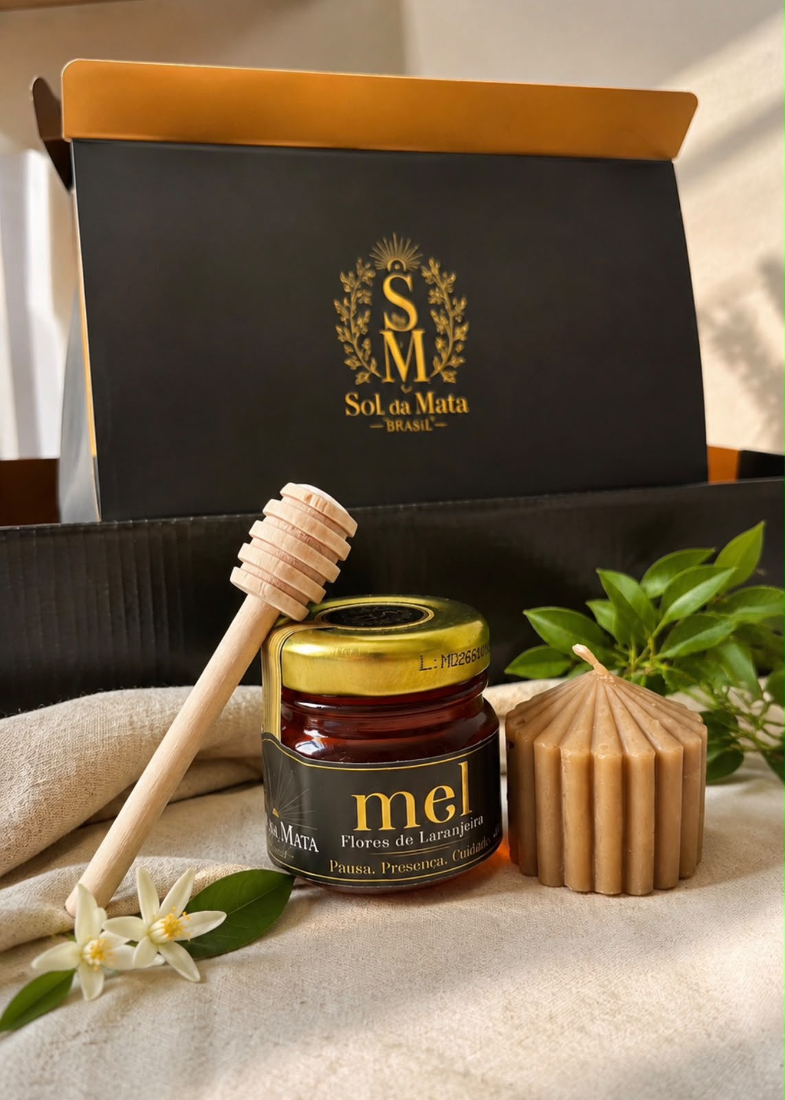 Kit Mel + Vela com mel Flores de Laranjeira, vela natural de cera de abelha e colher de mel, com caixa Sol da Mata ao fundo.